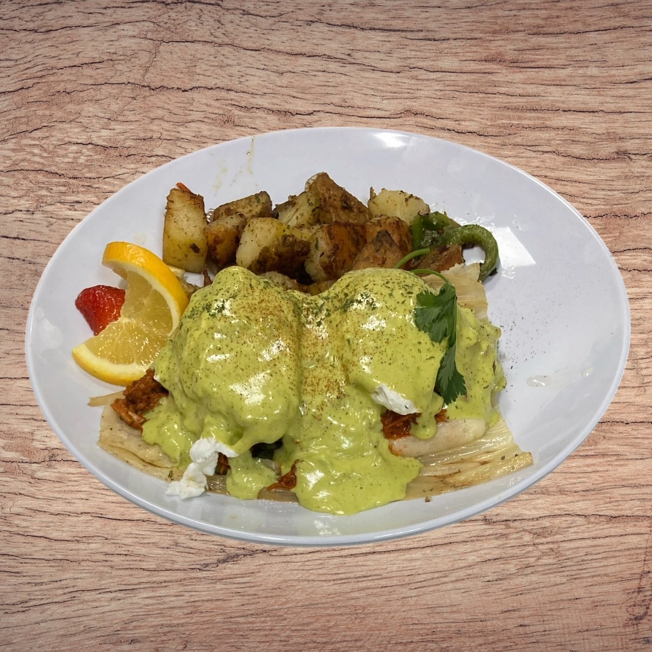 Eggs Benedict with potatoes, lemon, and strawberry on a white plate.