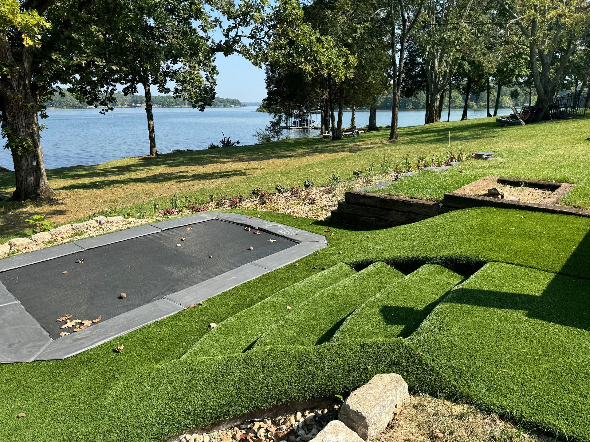 A trampoline is sitting on top of a lush green lawn next to a lake.