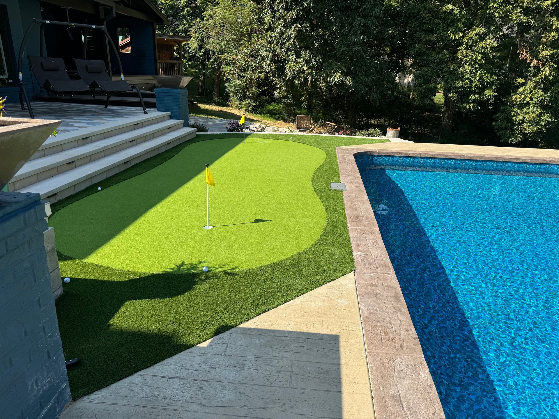 There is a putting green next to a swimming pool.