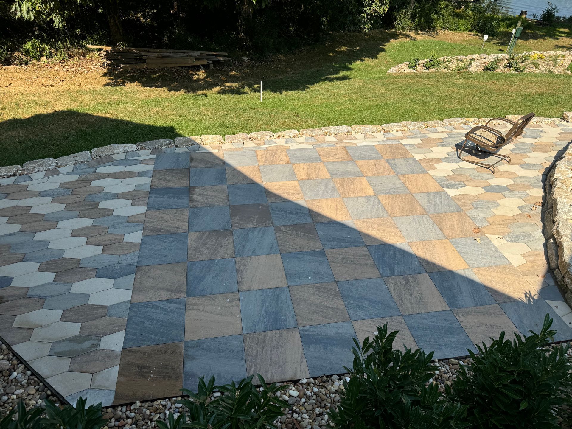 A patio with a checkered pattern and a chair in the grass.
