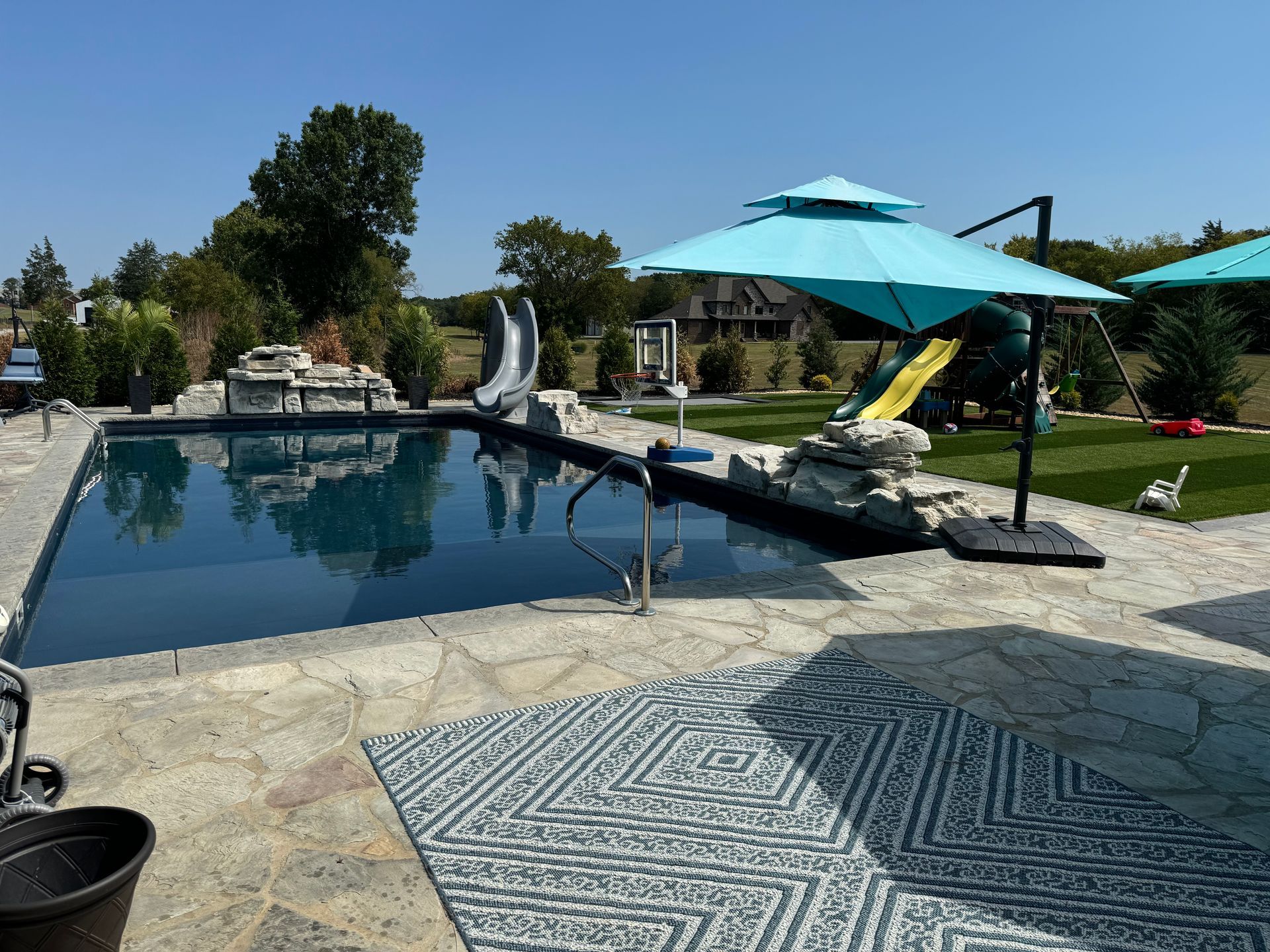 A large swimming pool surrounded by umbrellas and a slide.