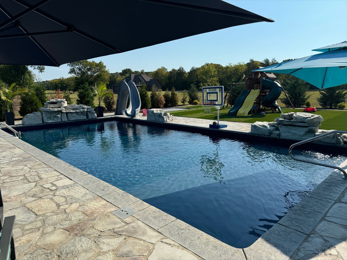 A large swimming pool surrounded by umbrellas and a playground