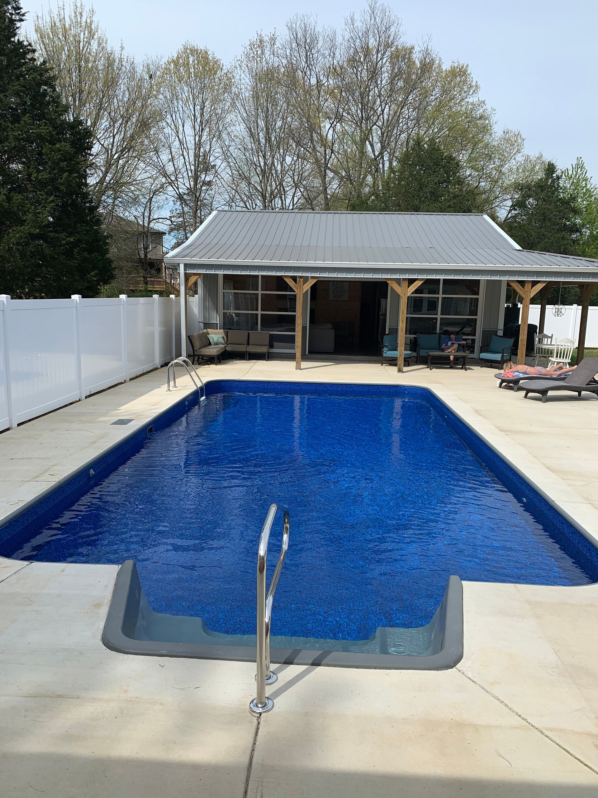 A large swimming pool is surrounded by chairs and a white fence.