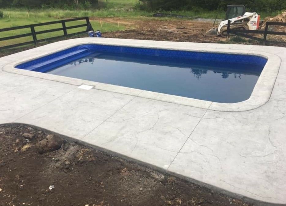 A large swimming pool with a concrete patio and a fence in the background.