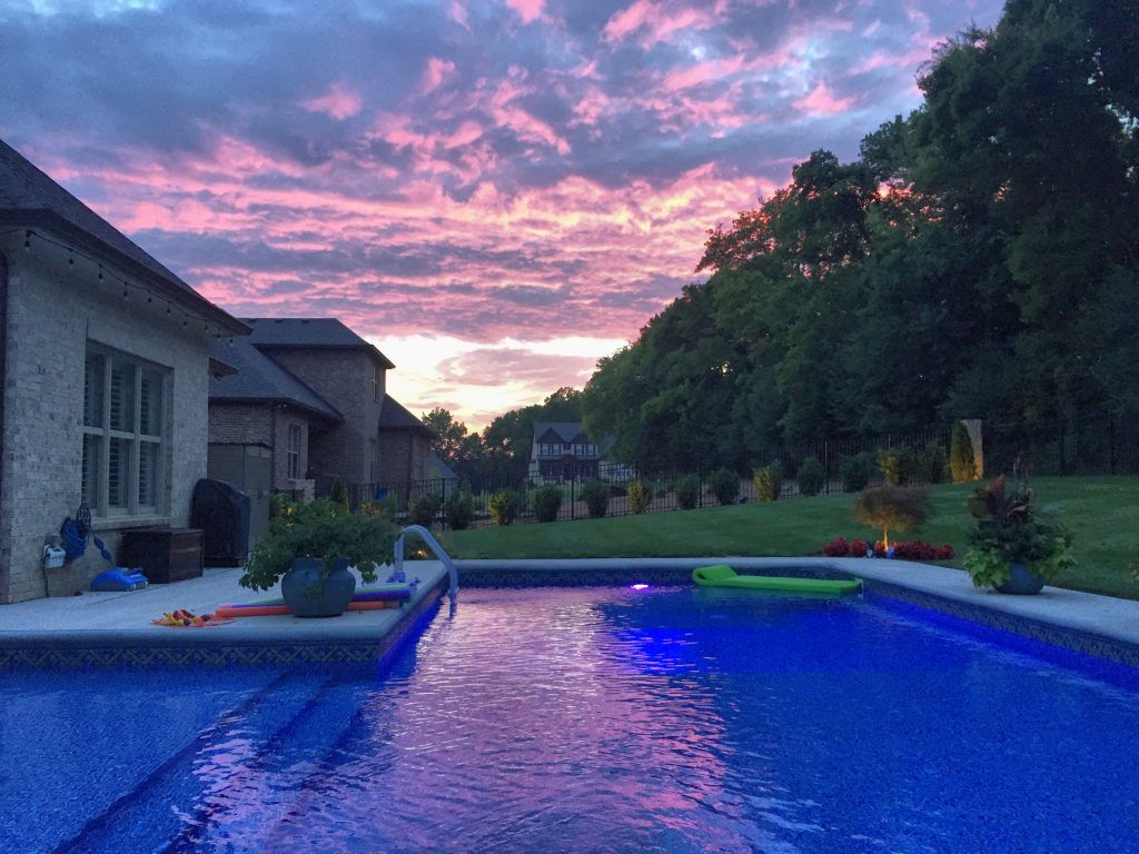 A swimming pool with a sunset in the background and a house in the background.