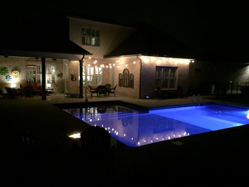 A large swimming pool is lit up at night in front of a house.