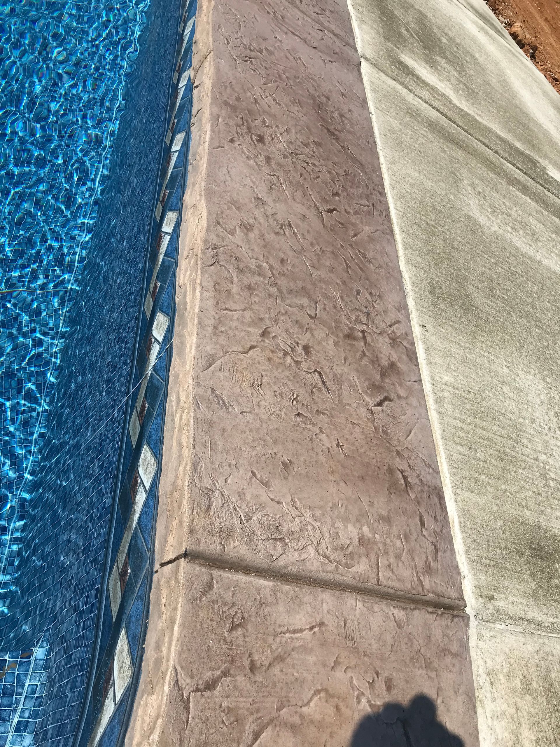 A close up of a concrete border next to a swimming pool.