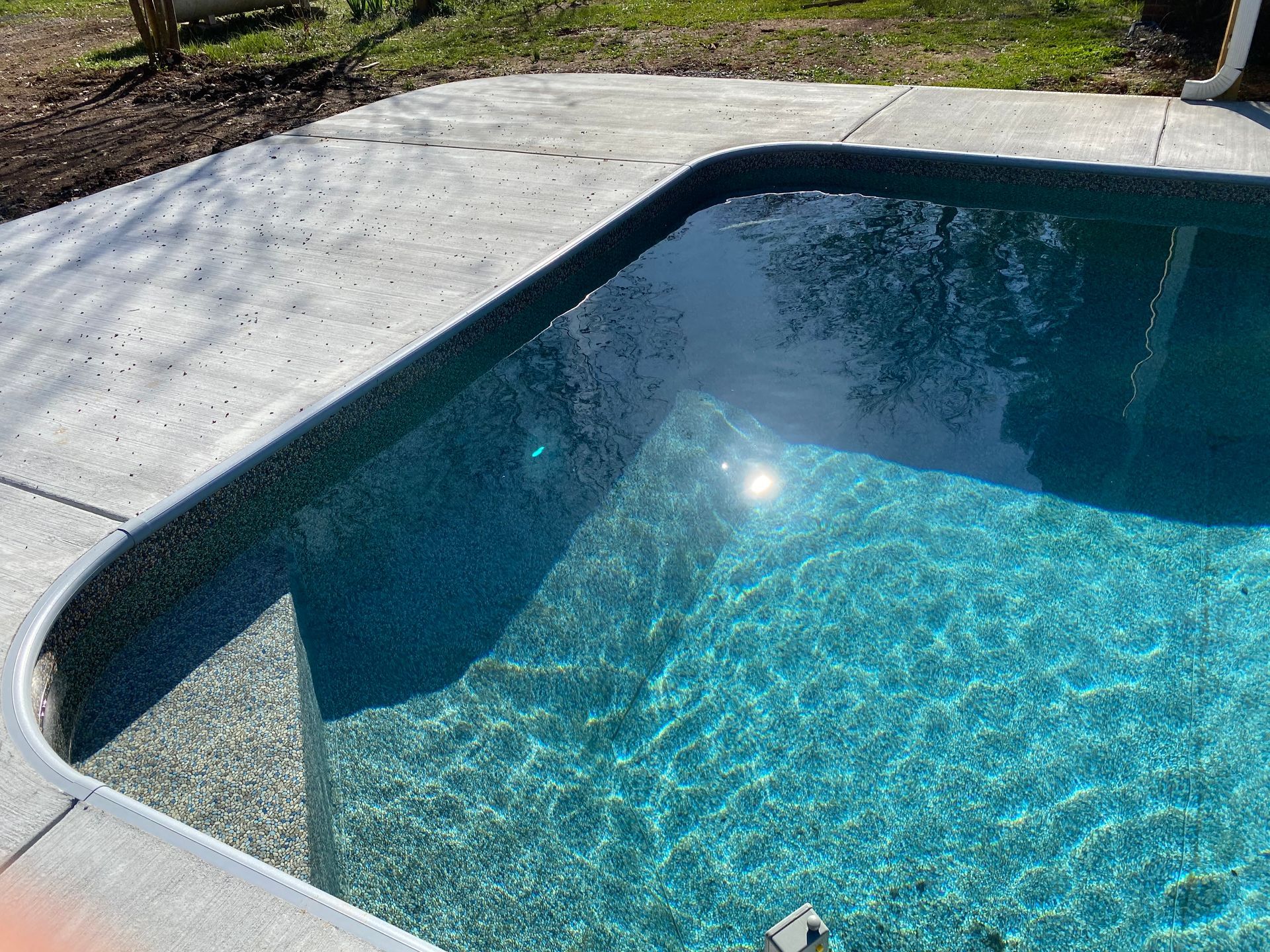 A swimming pool with a concrete border and a reflection of trees in the water.