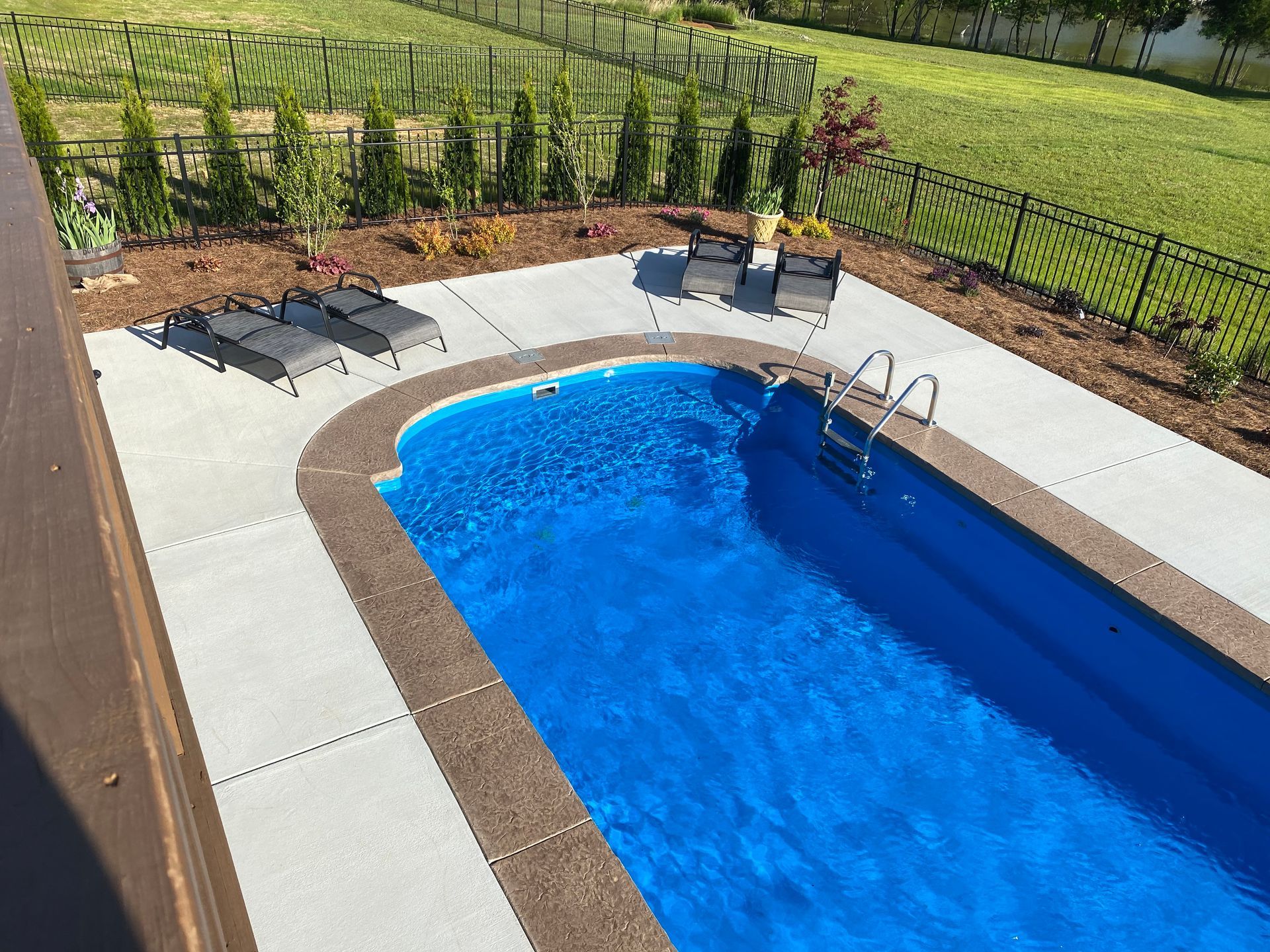 A large blue swimming pool is surrounded by chairs and a fence.