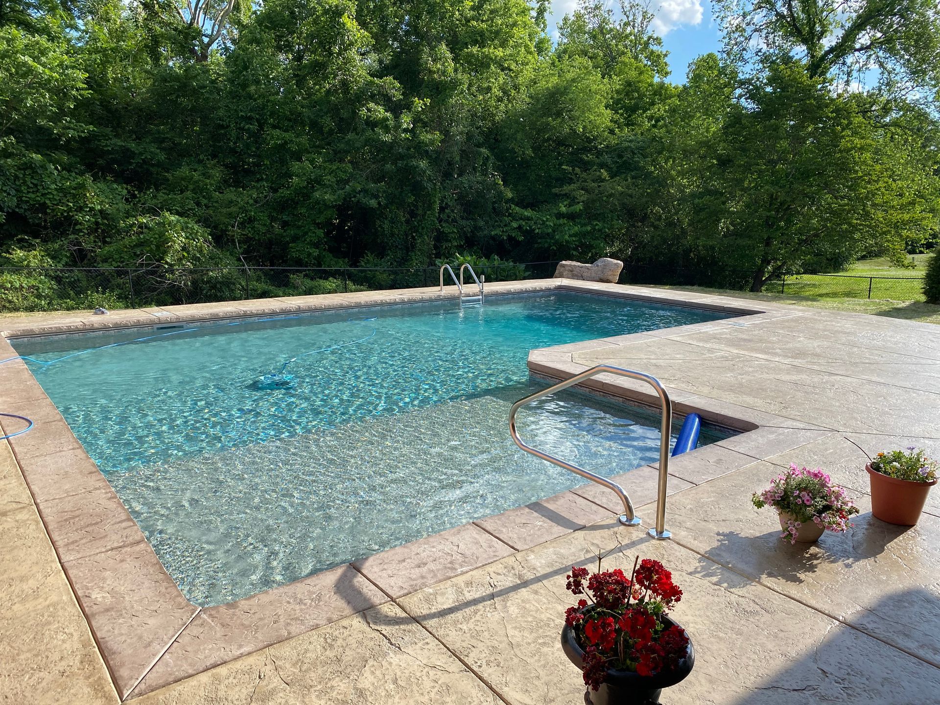A large swimming pool is surrounded by trees and a patio.