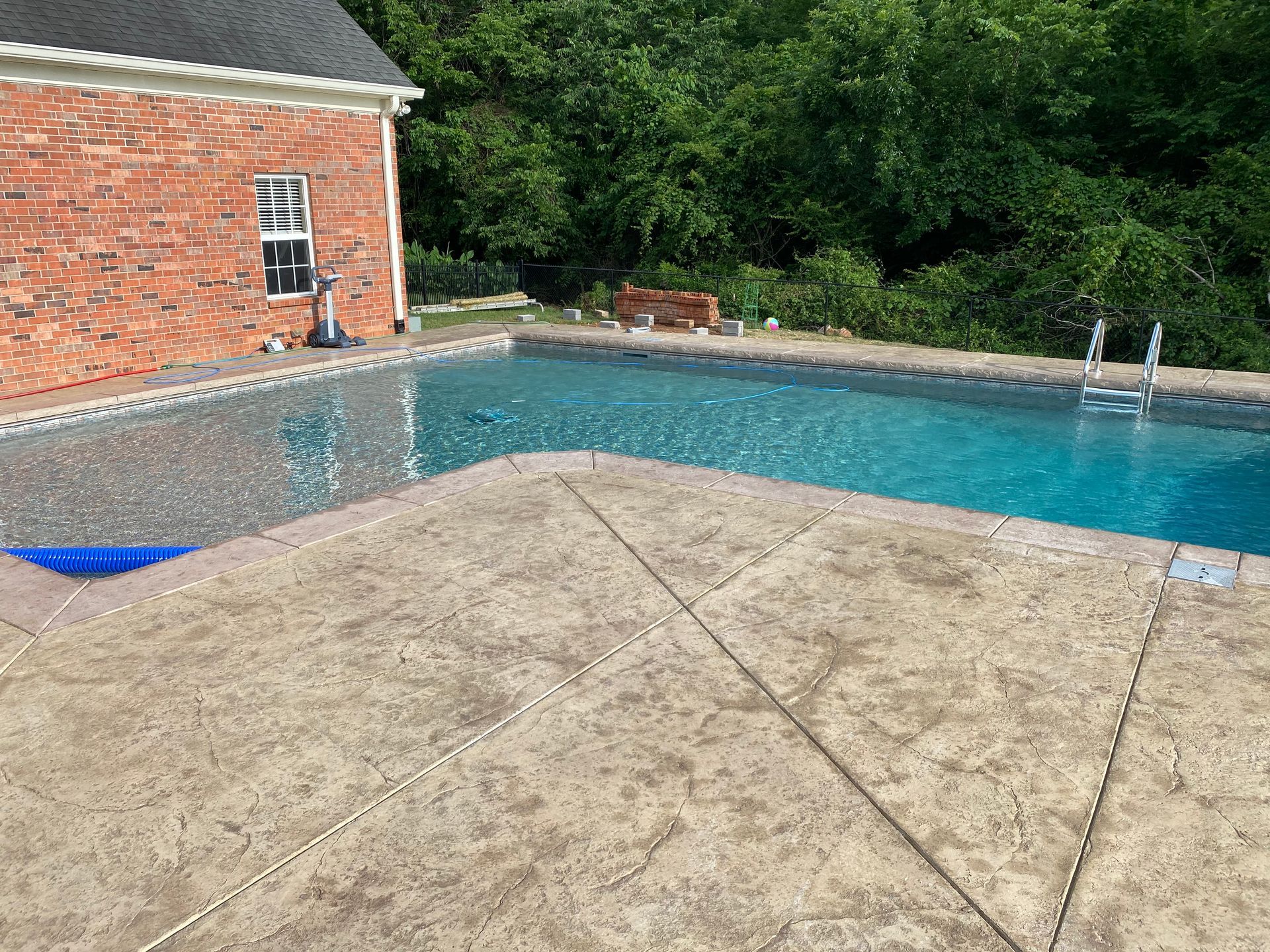 A large swimming pool is surrounded by trees and a brick building.