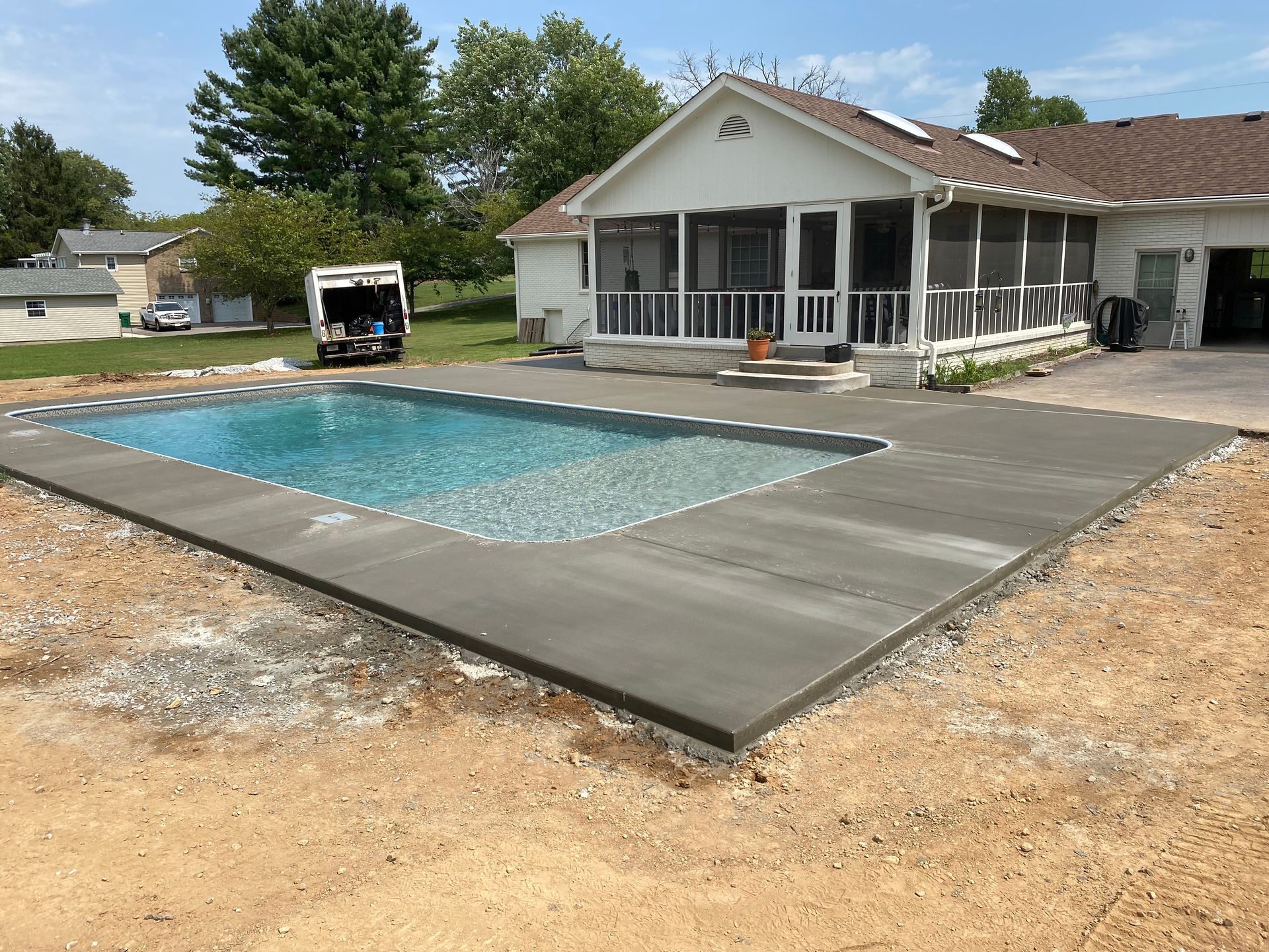 A swimming pool is being built in front of a house with a screened in porch.