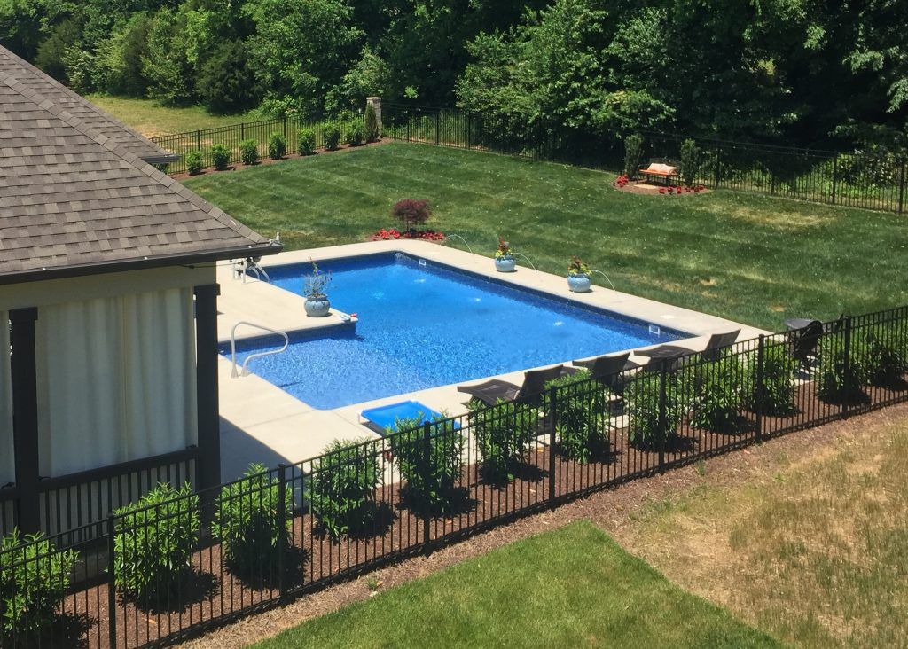 A large swimming pool is surrounded by a fence in a backyard.
