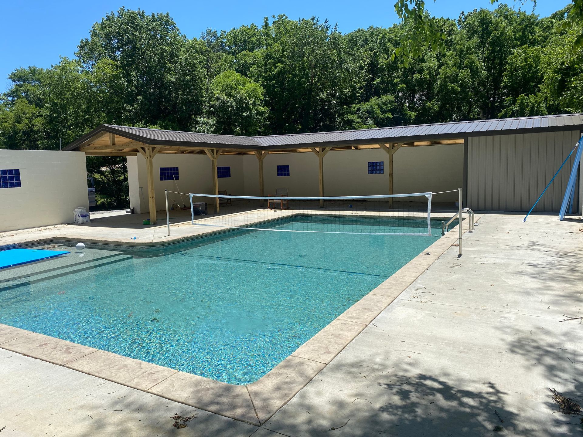 A large swimming pool is surrounded by trees and a covered area.