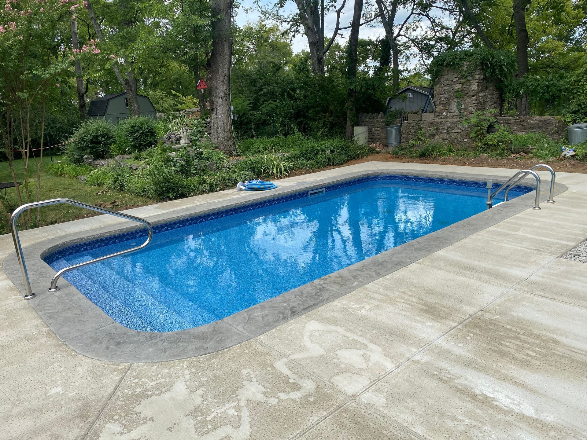 A large swimming pool is surrounded by trees and a concrete patio.