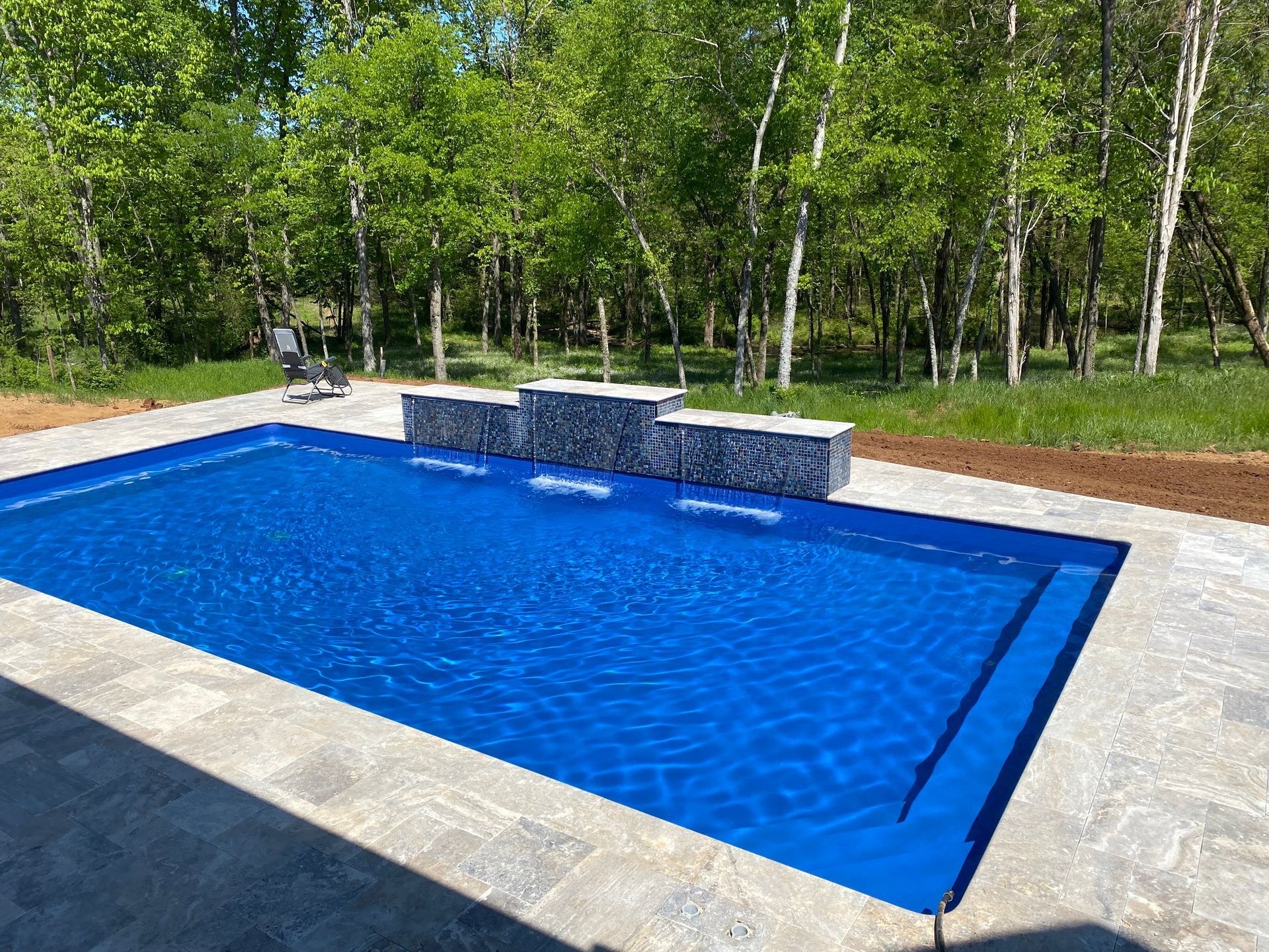 A large blue swimming pool surrounded by trees in a backyard.