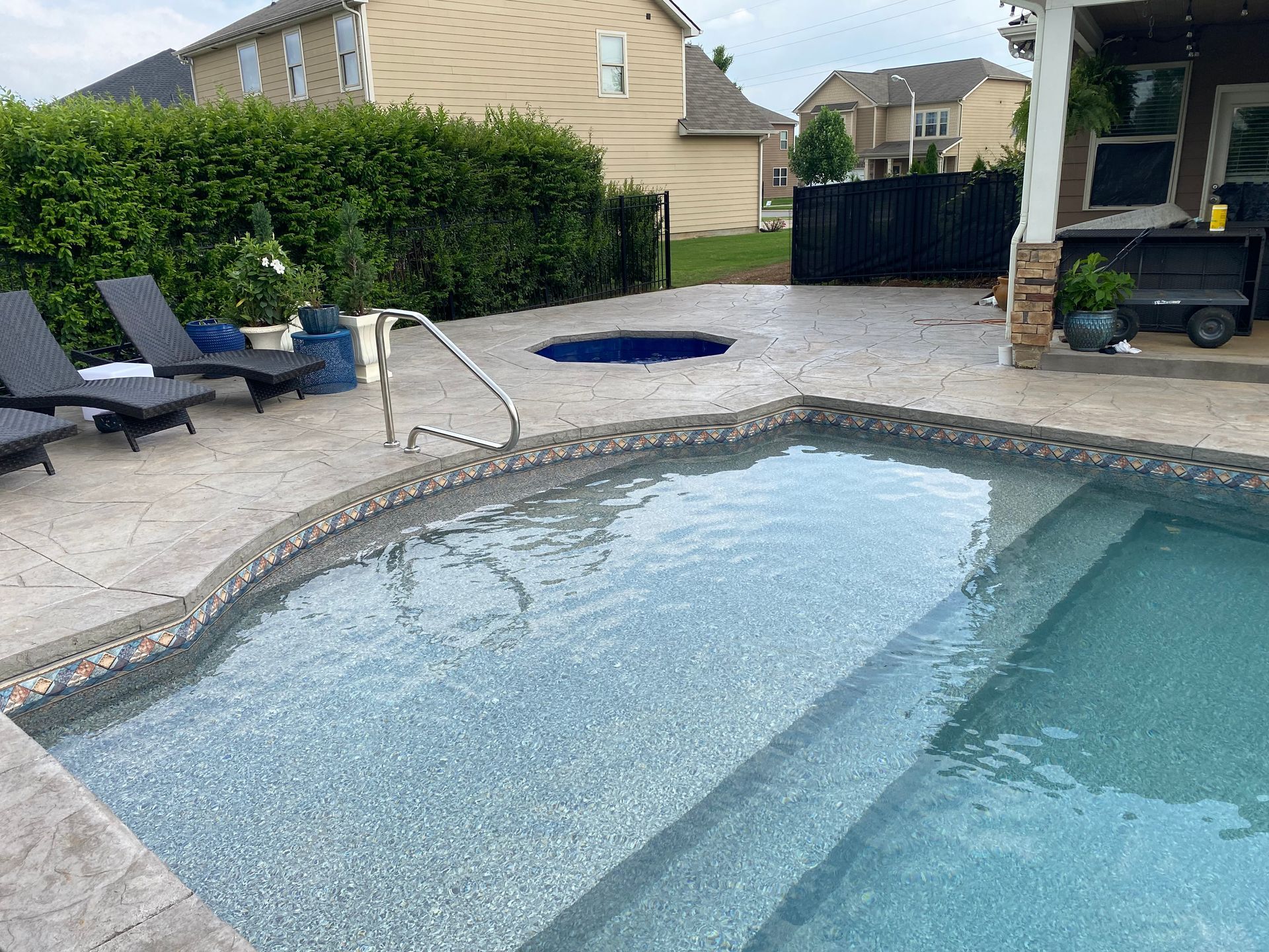 A large swimming pool with stairs and a hot tub in the backyard.