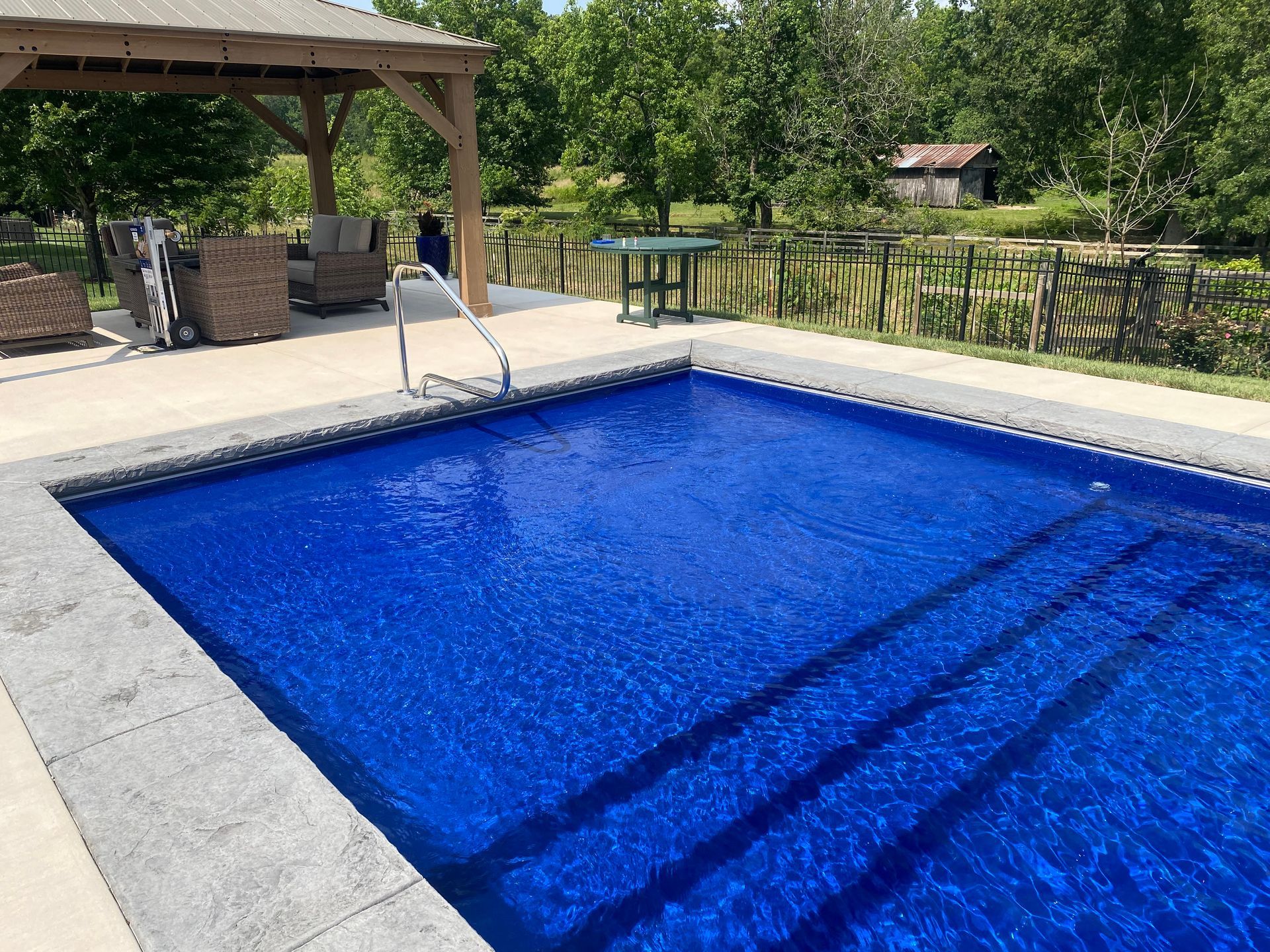 A large blue swimming pool with stairs and a gazebo in the background.