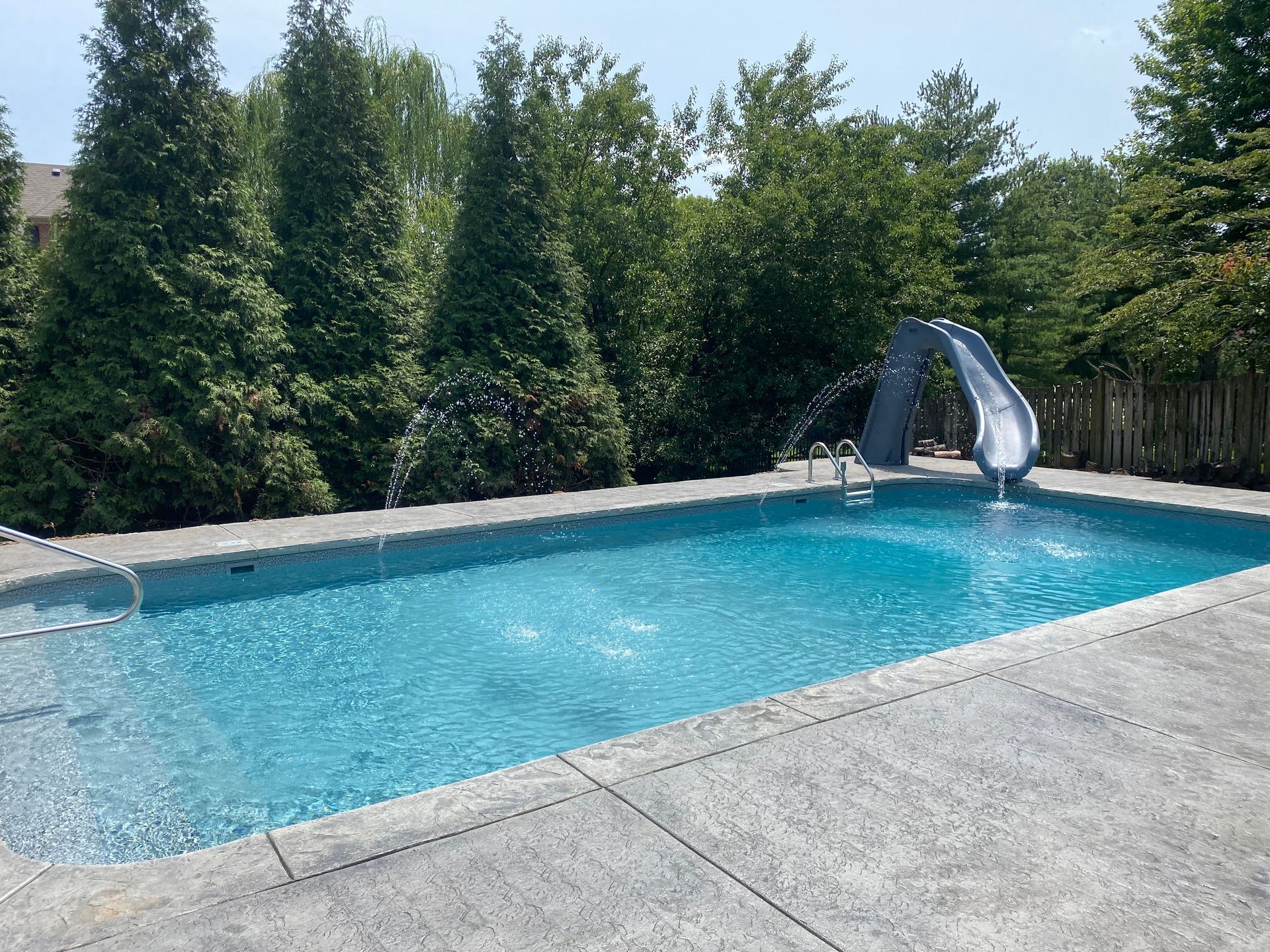 A large swimming pool with a slide attached to it surrounded by trees.