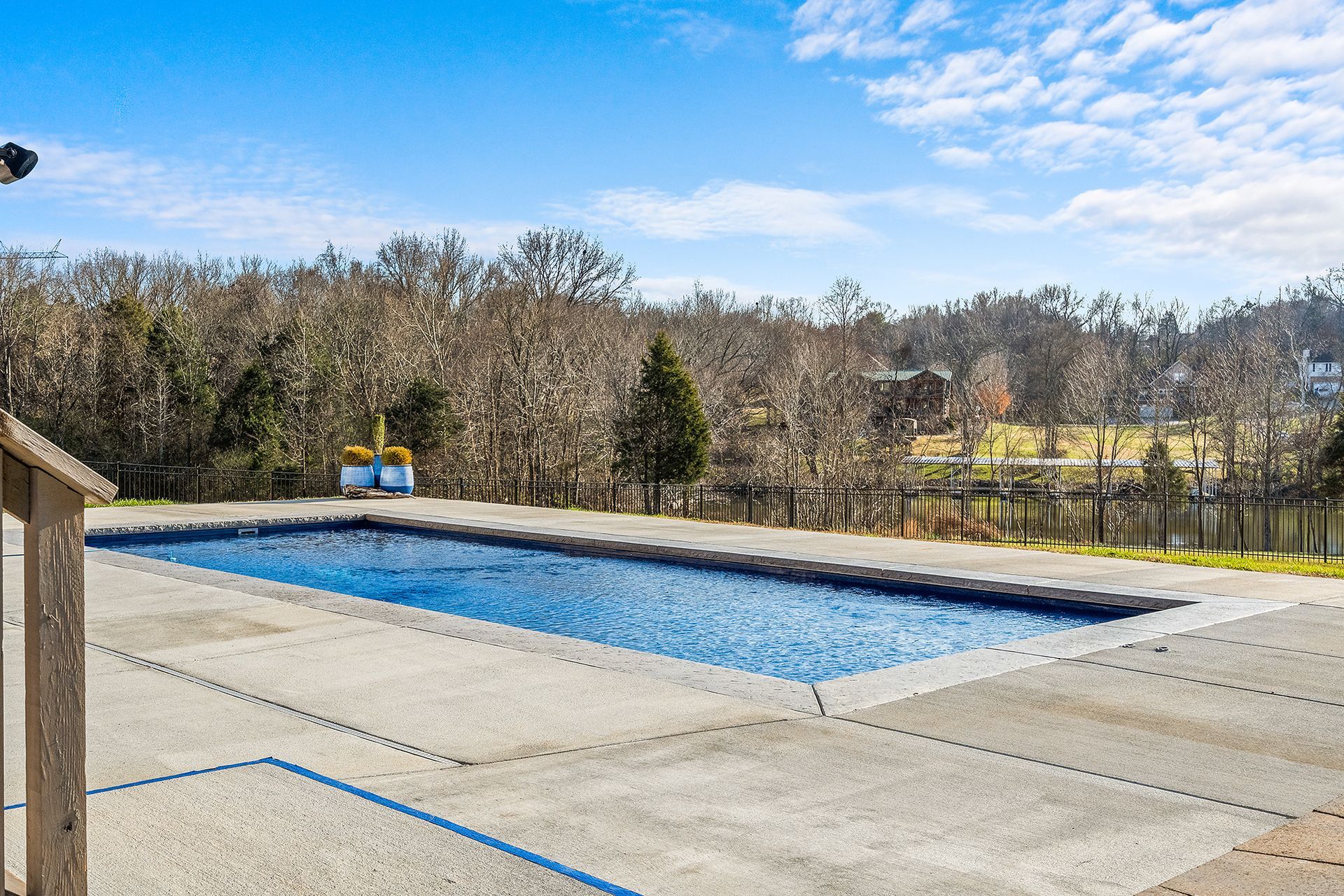 A large swimming pool is surrounded by trees and a fence.