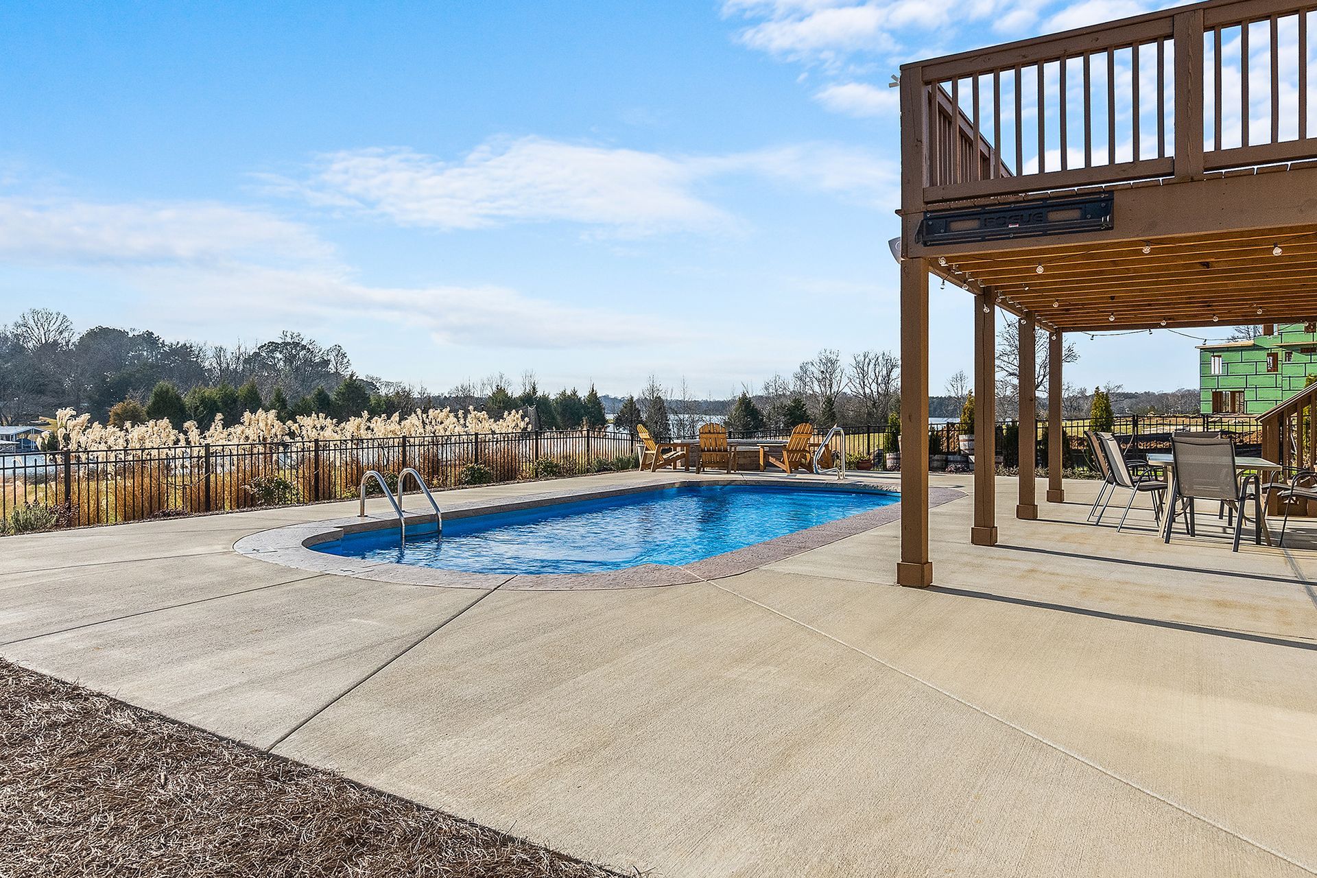 A large swimming pool is surrounded by a pergola and chairs.