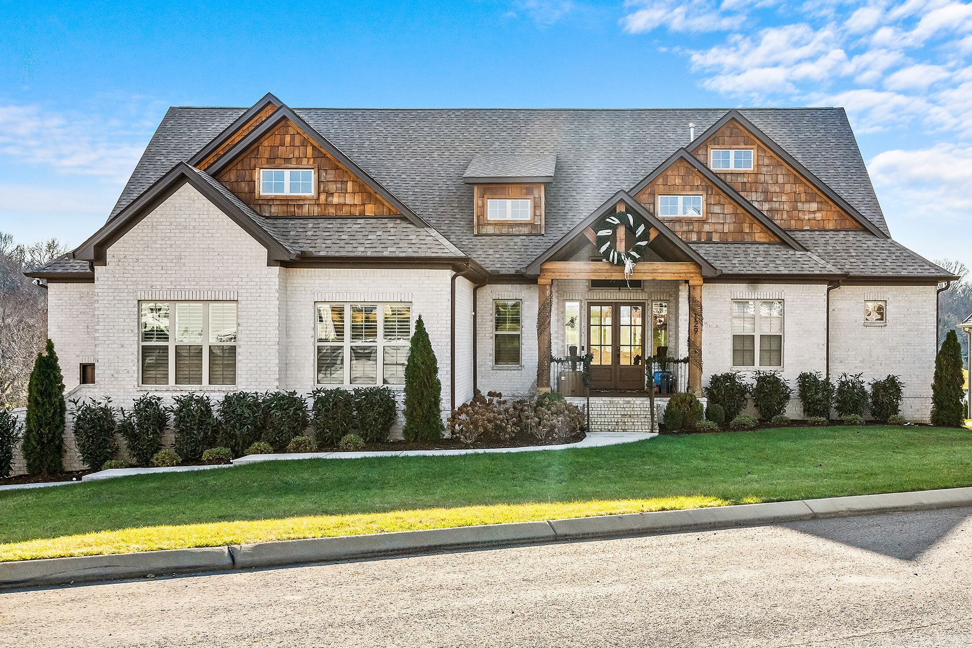 A large white house with a gray roof is sitting on top of a lush green lawn.