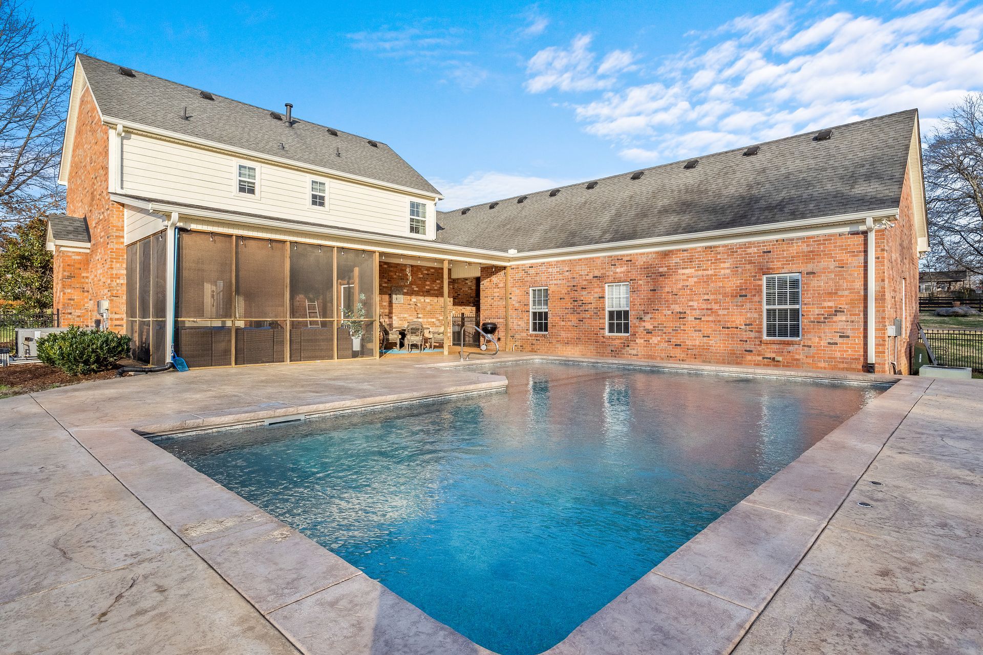 A large swimming pool is in the backyard of a brick house.