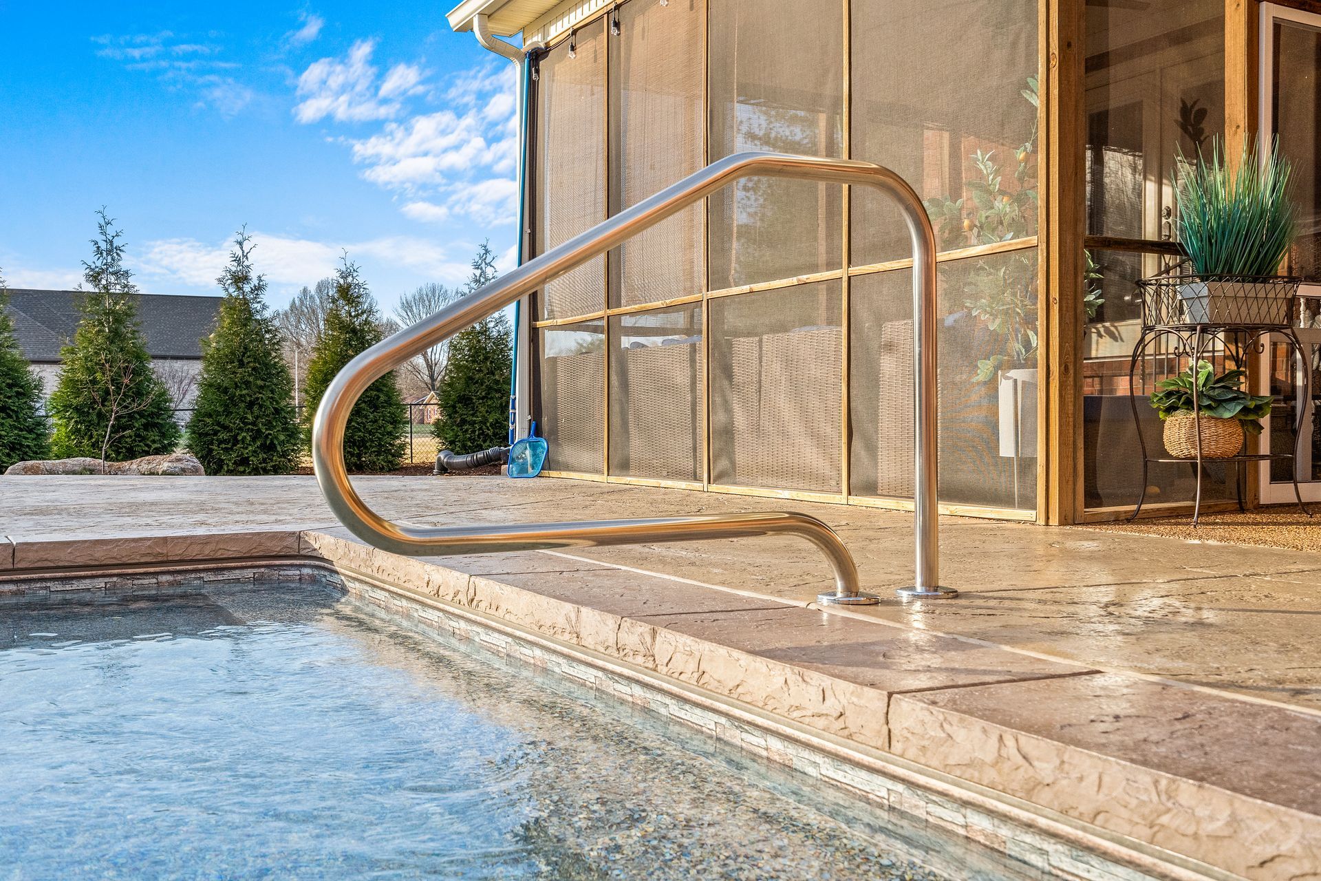 A swimming pool with a stainless steel railing and a screened in porch.
