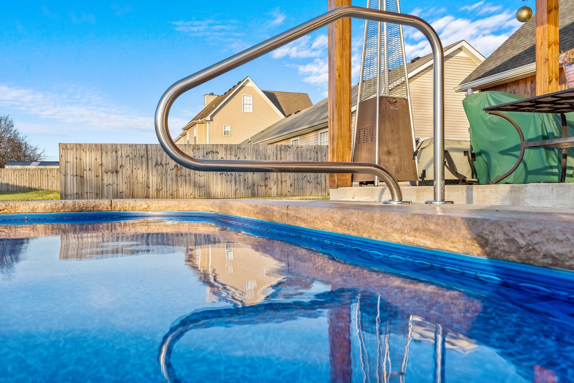 A swimming pool with stairs leading to it and a reflection of a house in the water.