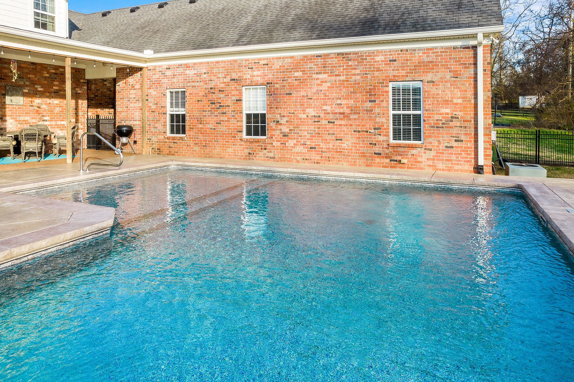 A large swimming pool in front of a brick house.