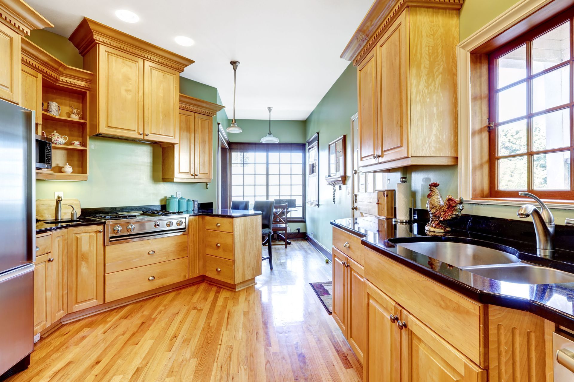 Kitchen with wooden cabinets, black countertops, stainless steel appliances, and wood flooring.