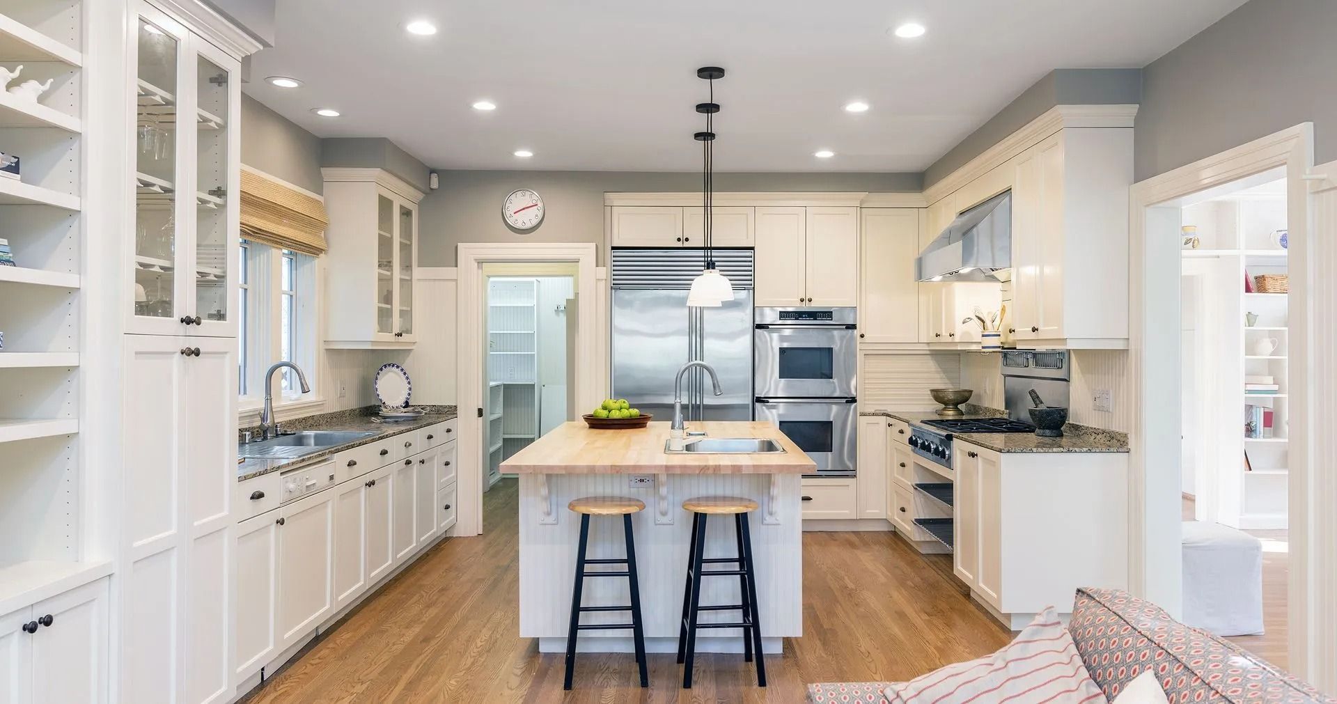 Cream-colored kitchen with a stainless steel refrigerator, island, and wooden floors.