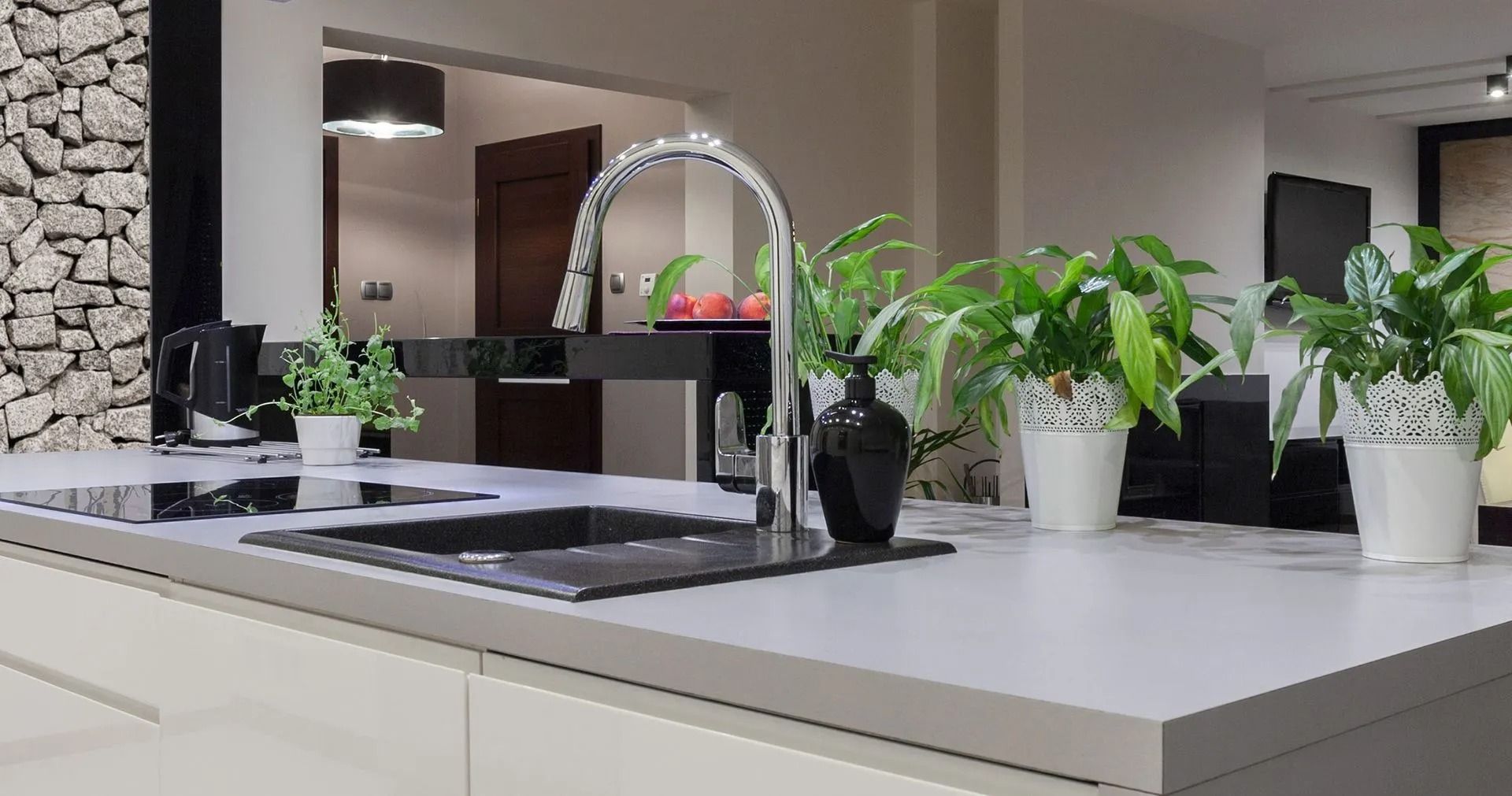 Kitchen island with sink, faucet, plants, and stone wall in modern design.