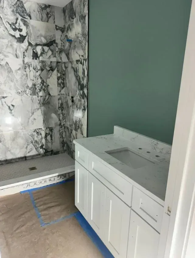 Bathroom under construction; white vanity and marble shower, teal wall.