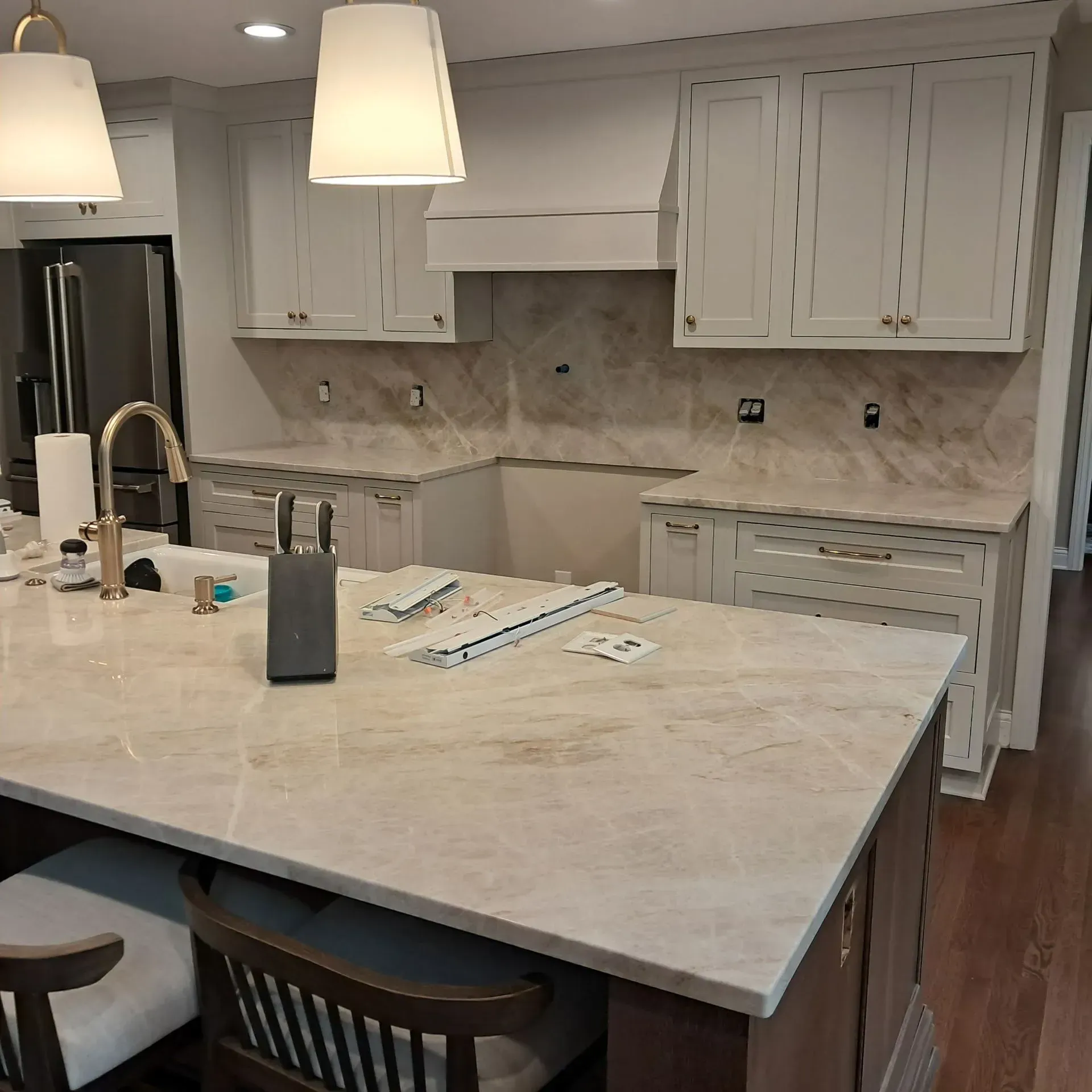 Kitchen with light-colored cabinets, marble countertops, island with seating, and gold faucet.
