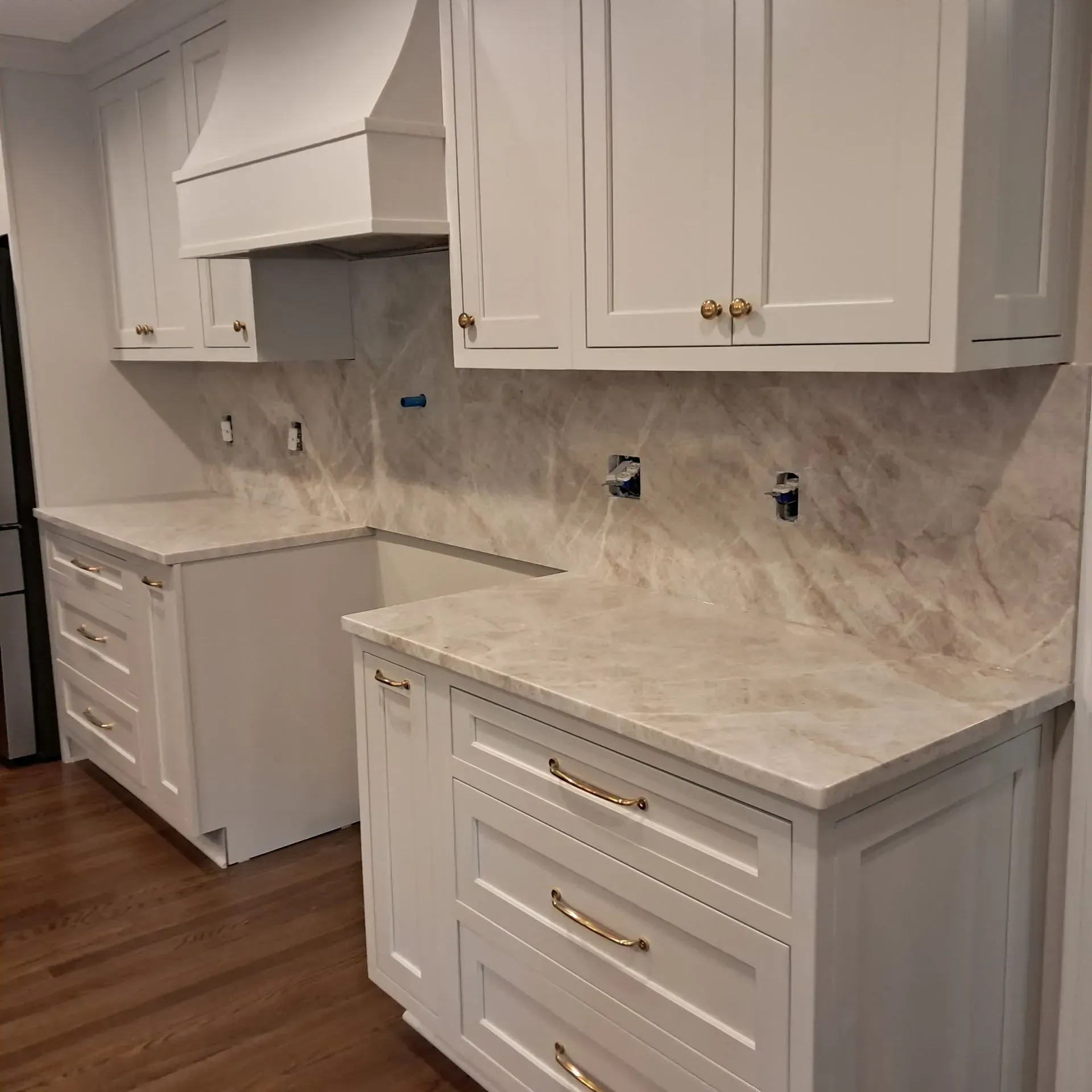 White kitchen cabinets with light countertops and backsplash. Brass hardware.