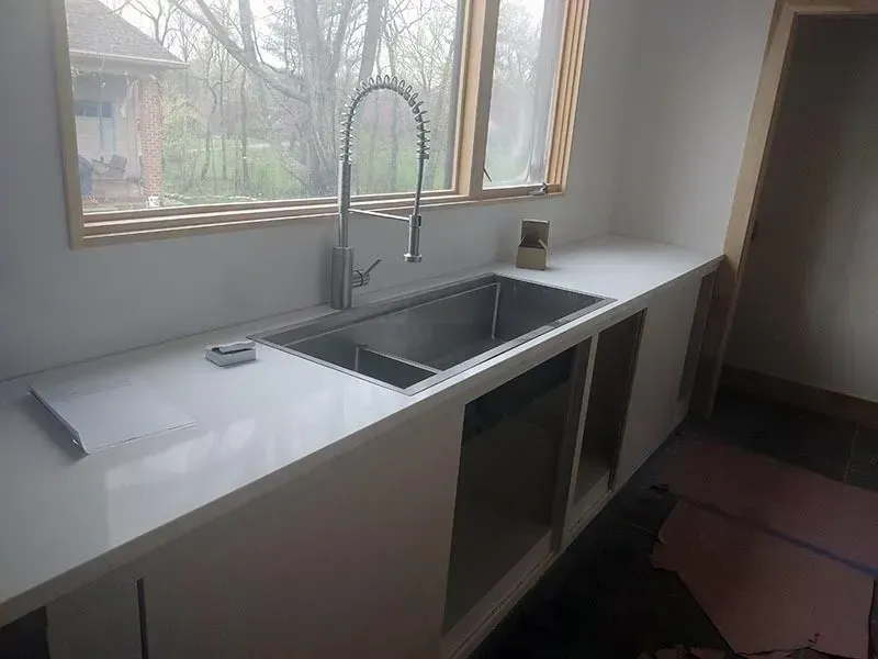 Kitchen with a stainless steel sink, white countertop, and window. Cabinet frames are visible.