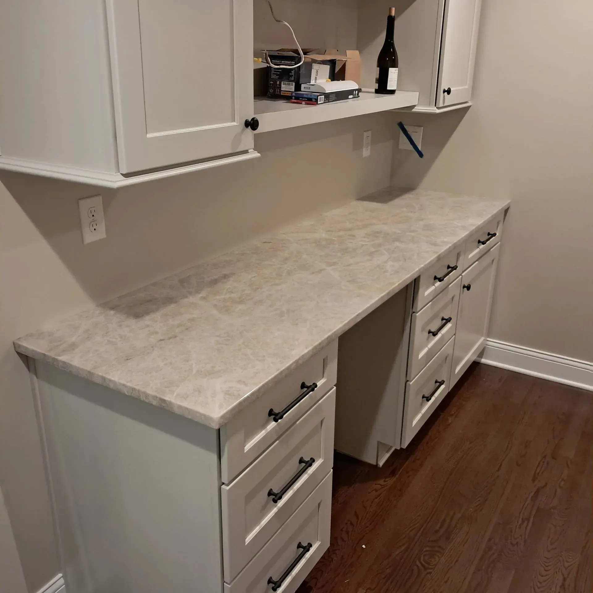 Built-in desk with cabinets, light grey countertop, dark drawer pulls, and hardwood floor.