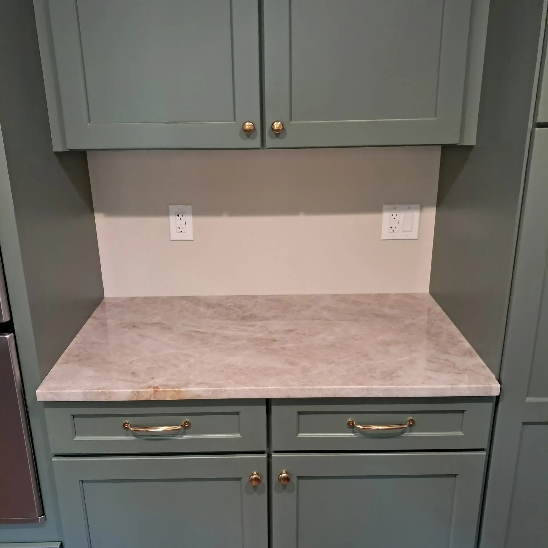 Green kitchen cabinetry with a countertop, electrical outlets, and brass hardware.