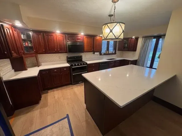 Newly renovated kitchen with dark wood cabinets, white countertops, and a large island.