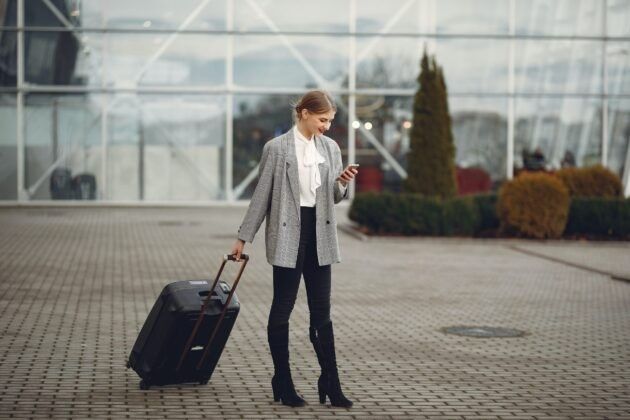 A woman is walking with a suitcase and looking at her phone.