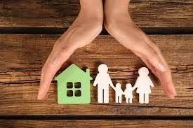 A person is holding a green house and paper cut outs of a family.