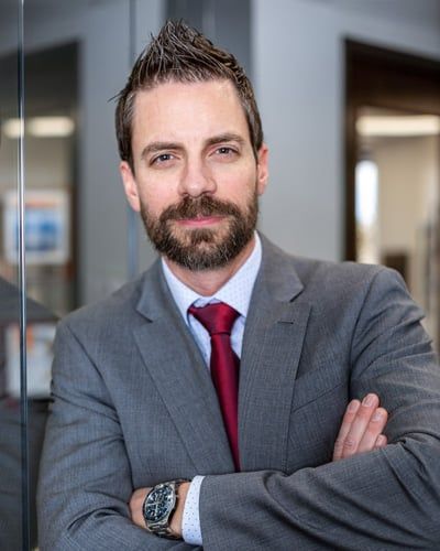A man in a suit and tie is standing with his arms crossed.