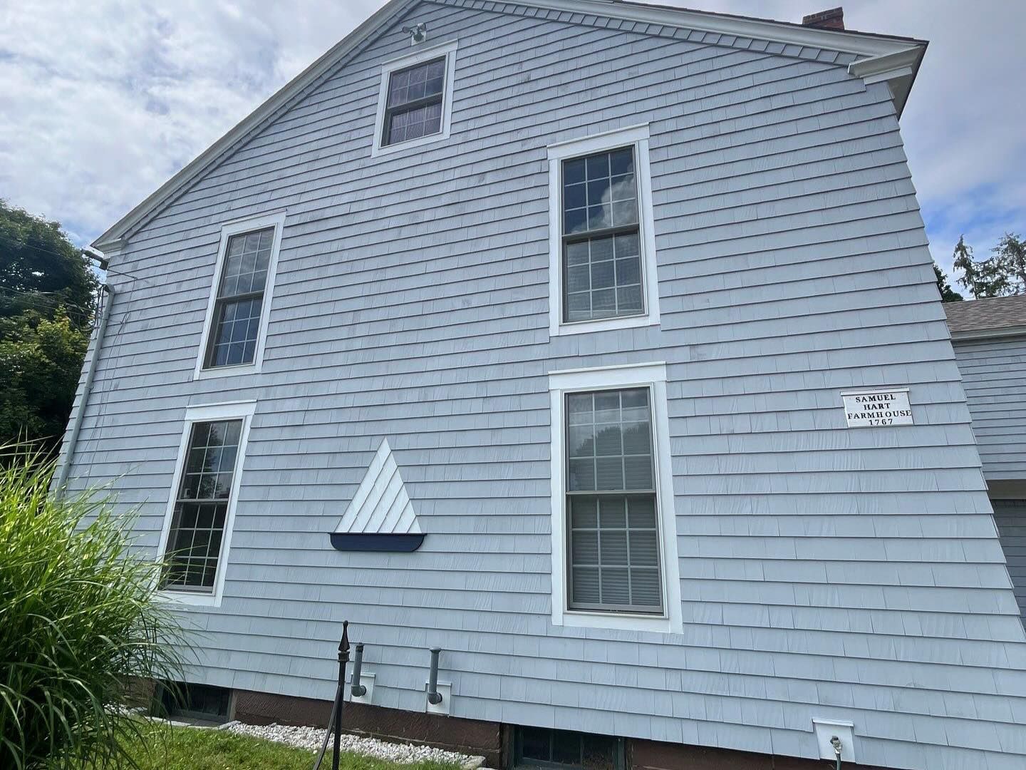 Light blue clapboard house with four tall windows, a triangular accent, and a small attic window.