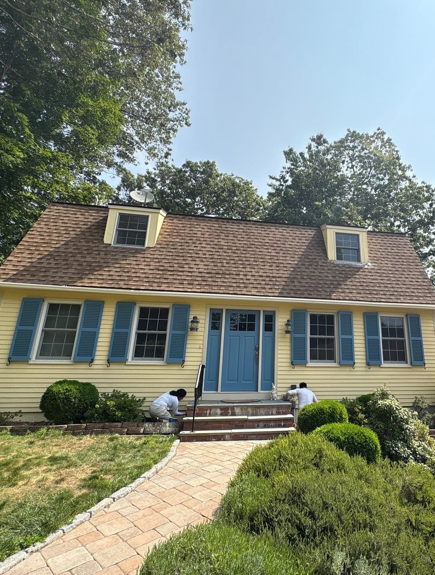 Yellow house with blue shutters and door, two people working on steps outside.