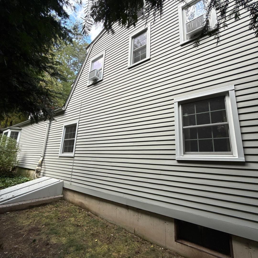Side view of a house with gray siding, white windows, and an angled roof.