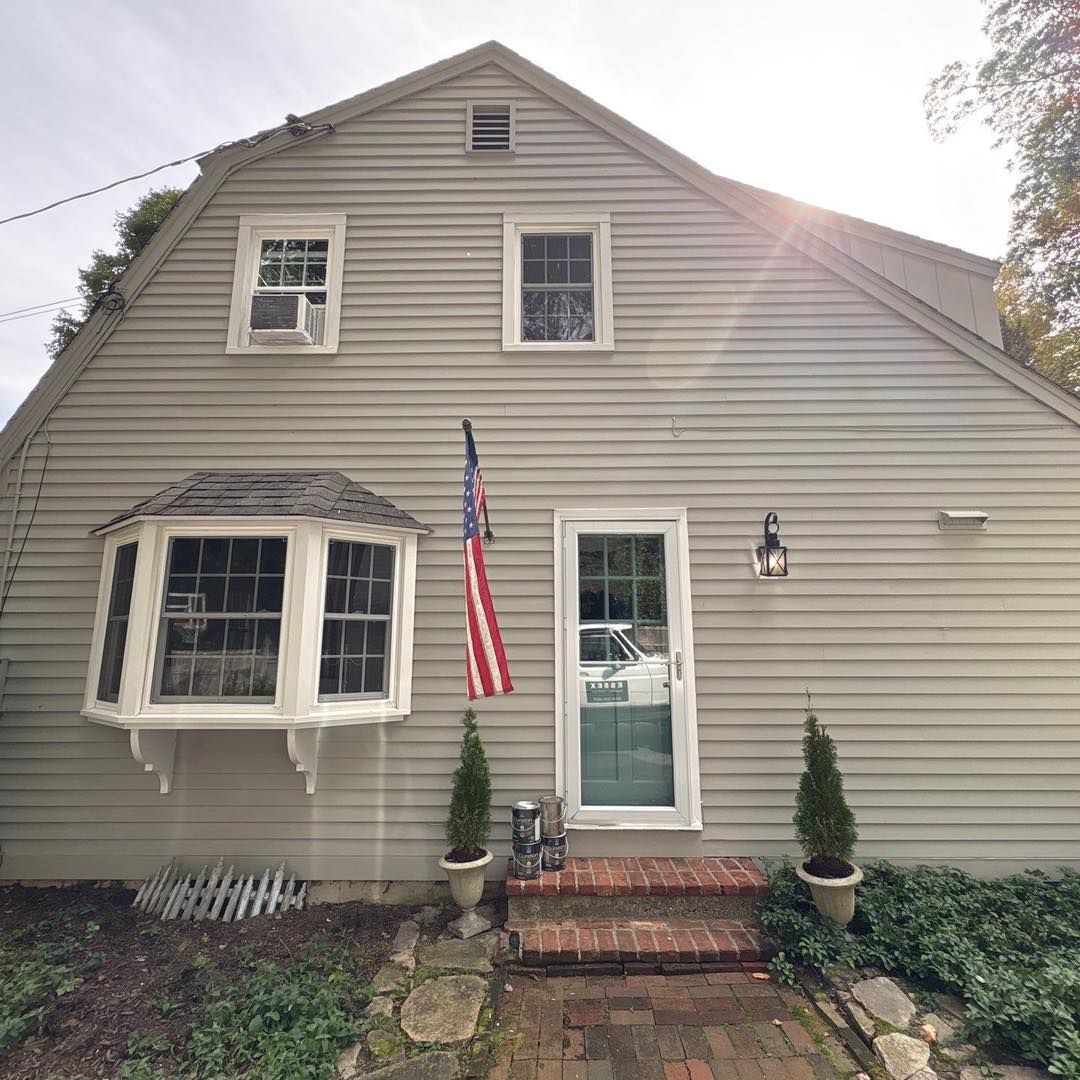 Gray house with bay window, American flag, and front door. Brick steps lead to the entrance.