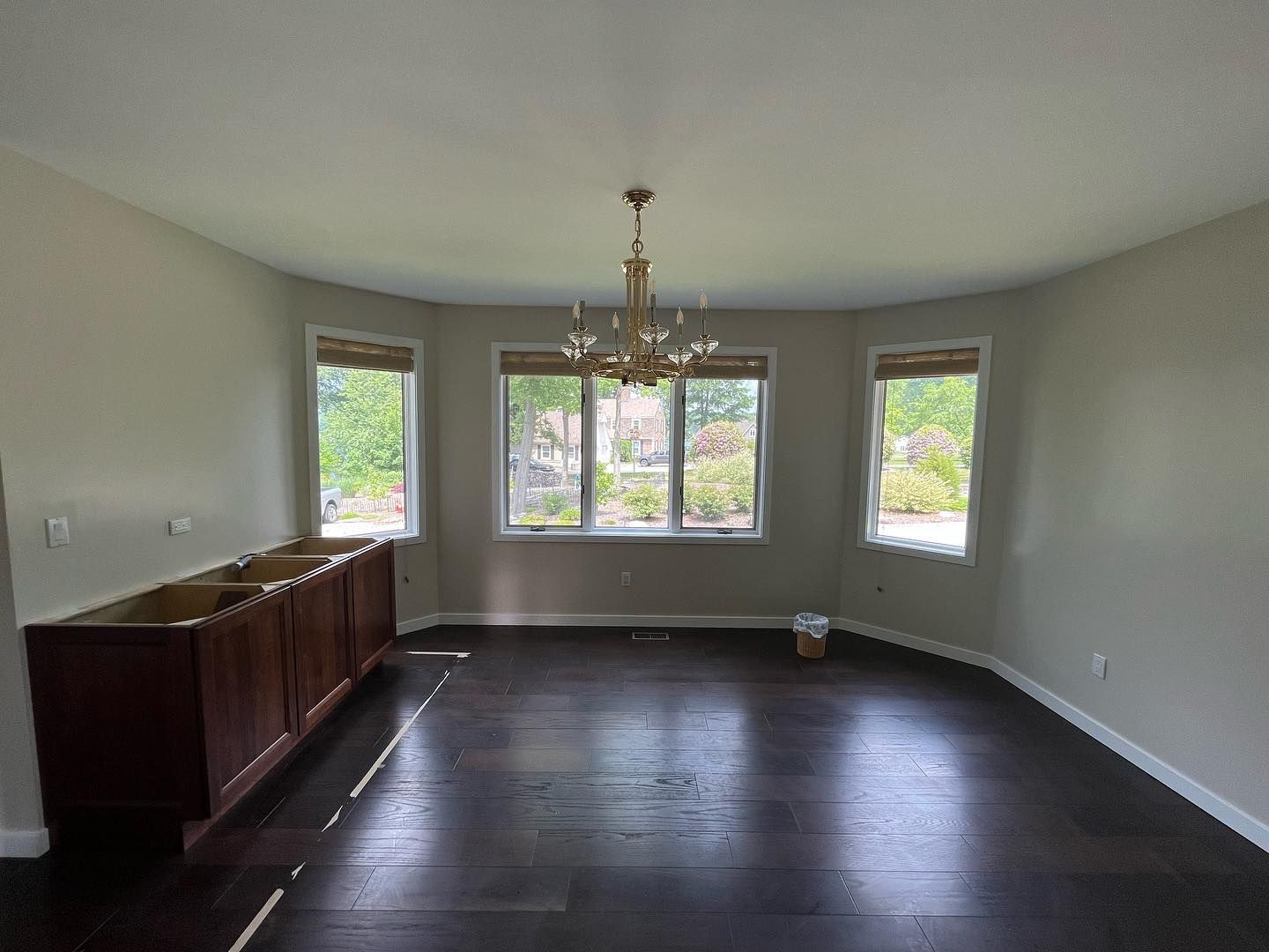 Empty dining room with dark wood floor, windows, and a chandelier. Cabinets on the left.