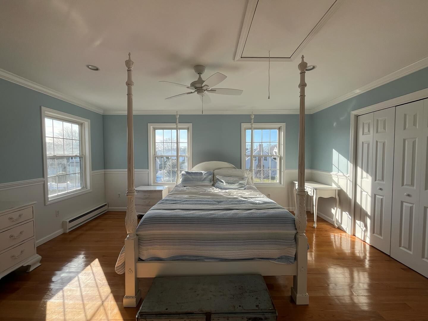 Bedroom with four-poster bed, blue walls, white trim, hardwood floors, natural light.