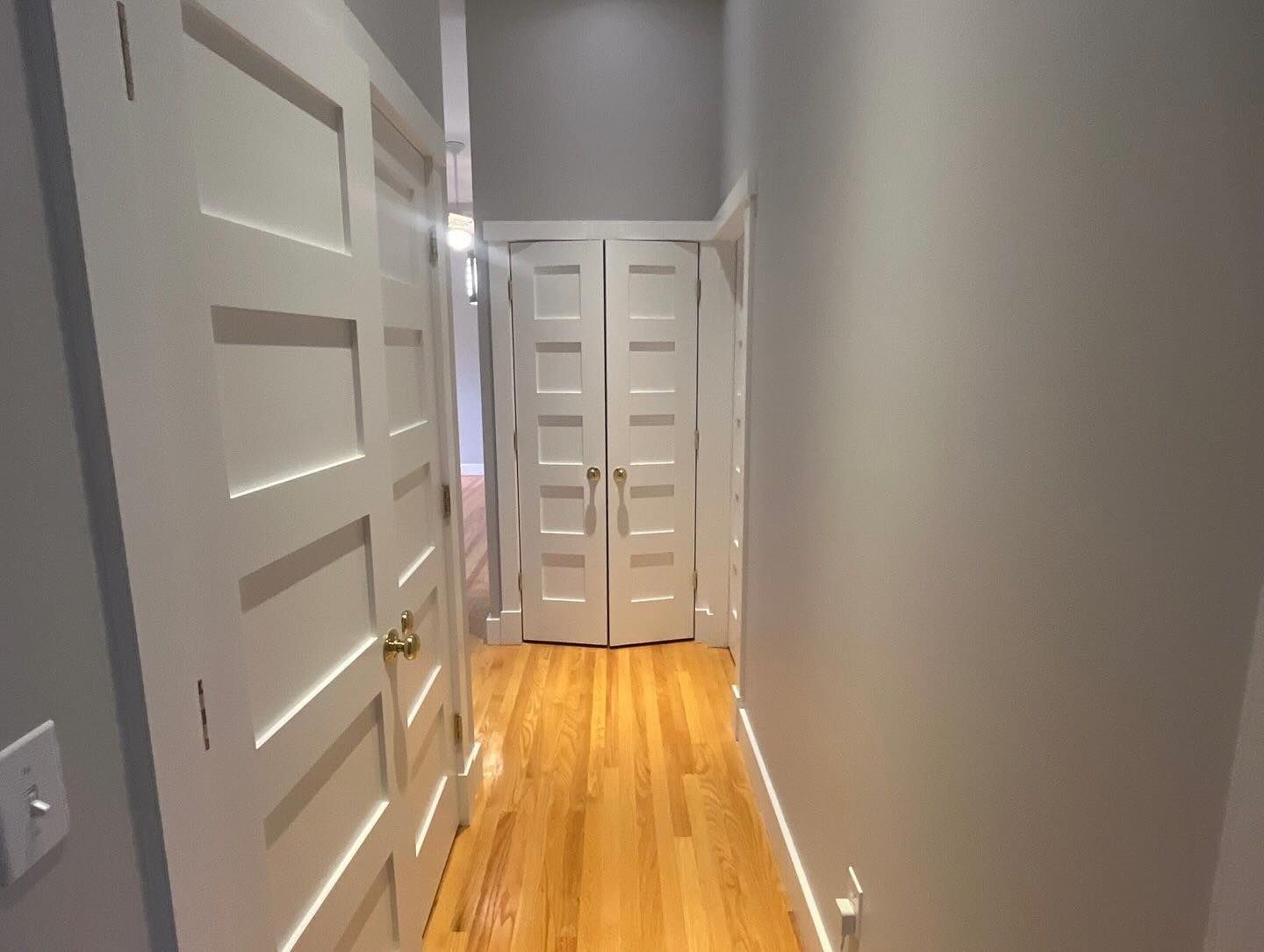 Narrow hallway with hardwood floor, white doors, and light gray walls.